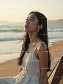 Elegant Woman in White Dress Sitting by Relaxing Seaside Landscape
