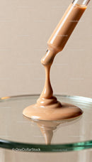 Beige liquid foundation pouring from dropper into glass dish