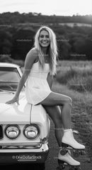 Smiling woman in white dress with roller skates on car hood