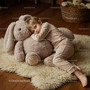 Child resting with oversized plush bunny on cozy rug