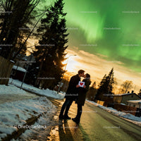 Couple sharing a kiss with heart card under northern lights