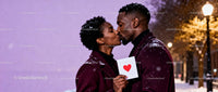 Affectionate couple kissing with Valentine card outdoors
