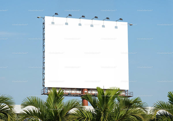 Large blank billboard above green palm trees under clear sky JPG Mockup Image