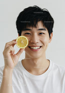 Smiling Young Man Holding Lemon Slice in Bright Casual Portrait