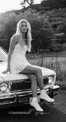Young woman in white dress sitting on vintage car with roller skates