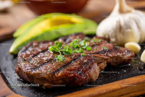 Juicy Grilled Beef Steak with Avocado and Garlic on Wooden Board