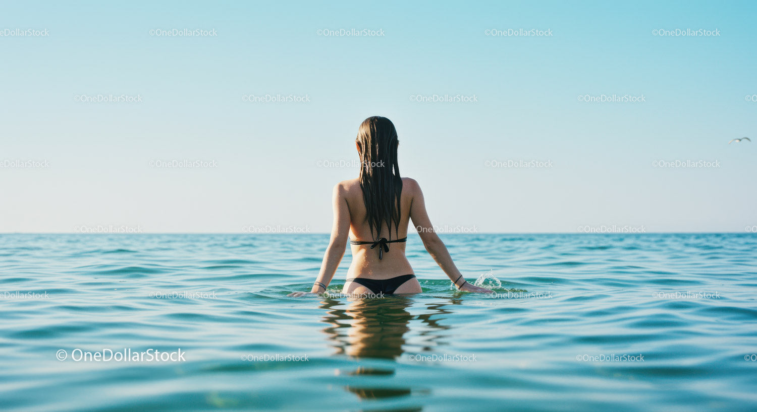 Kobieta w czarnym bikini pływa w spokojnym, błękitnym oceanie pod czystym niebem