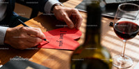 Man Writing Love Note on Red Heart Card by Wine Glass