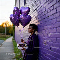 Woman holding heart balloons and chocolates by purple wall