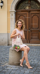 Smiling woman in pink dress holding a bag of fresh produce