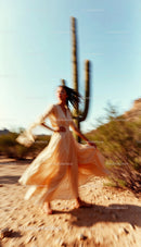 Carefree Woman in Flowing White Dress Dancing in Desert Landscape