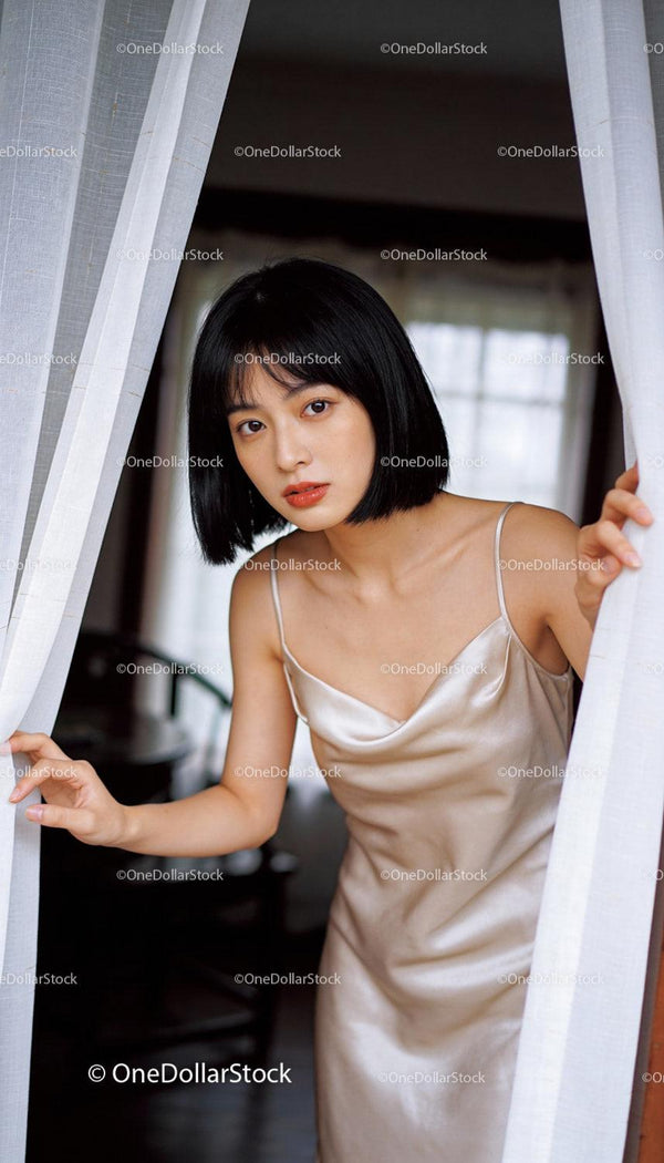 Young woman in satin dress peeking through curtains