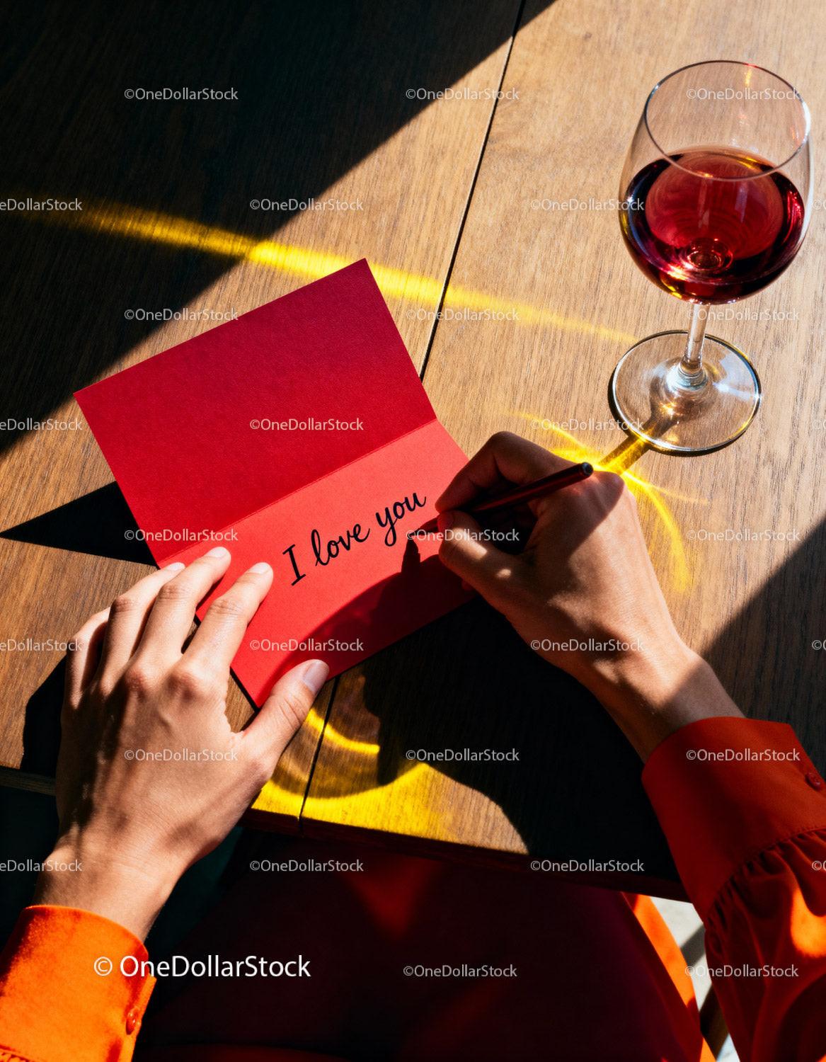 Person Writing I Love You in Red Card with Glass of Wine