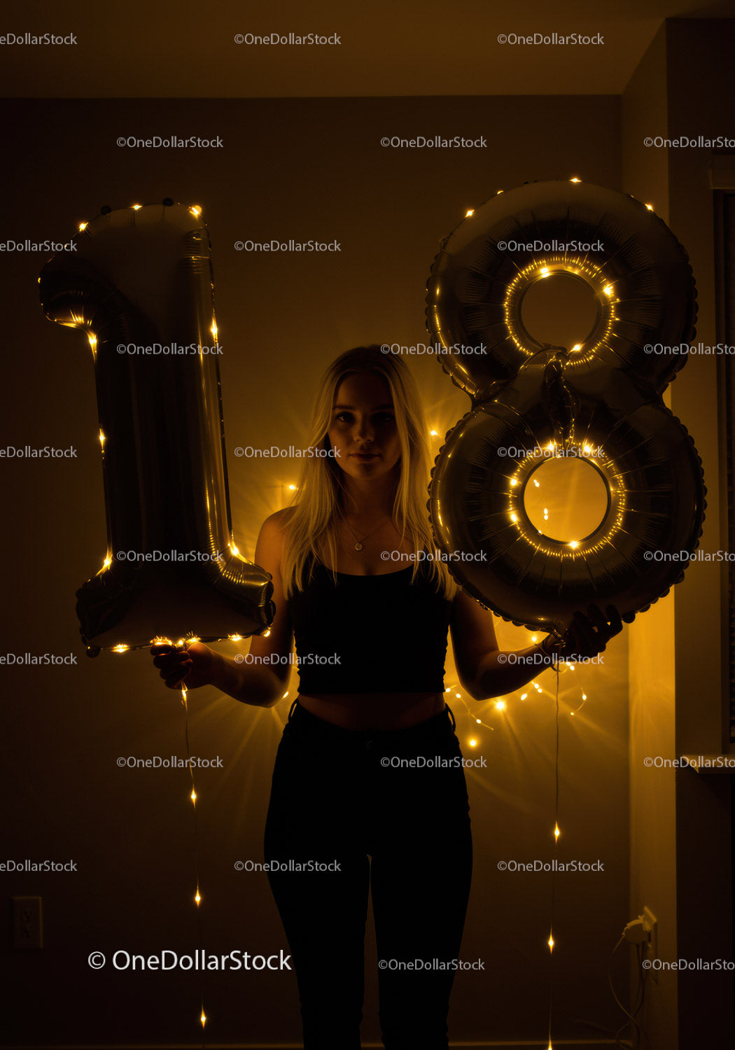 Young woman holding 18 balloon lights in dark room