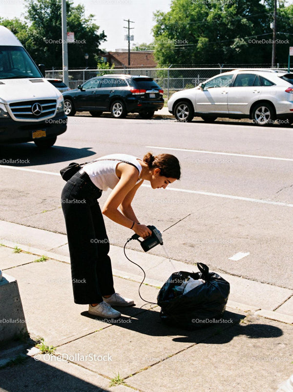Young woman using gadget to clean outdoor trash bag