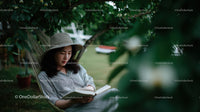 Woman Relaxing in Hammock Reading Book in Garden with Greenery