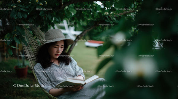 Woman Relaxing in Hammock Reading Book in Garden with Greenery