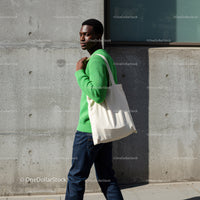 Young Man in Green Sweater with Tote Bag Standing Near Concrete Wall