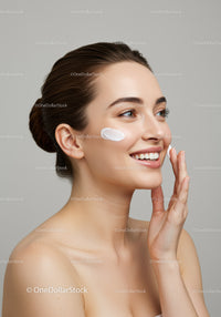 Young Woman Applying Skincare with Cream on Cheek in Studio
