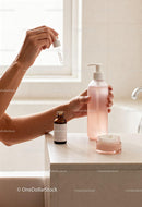 Hands applying serum with skincare bottles on marble