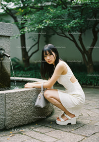 Fashionable Young Woman in White Dress Posing by Fountain in Park