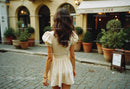 Woman in beige dress walking on cobblestone street in charming city scene