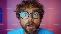 Young Man with Blue Glasses Showing Surprise with Pink Background