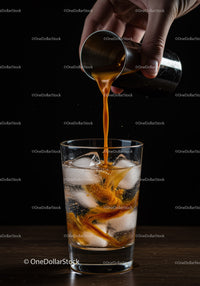 Pouring liquor into glass with ice cubes on dark background
