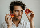 Young Man Holding Juicy Red Grapefruit Halves in Bright Indoor Setting