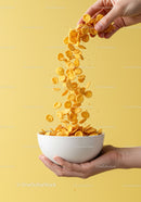 Hand Pouring Cornflakes into White Bowl on Yellow Background