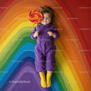Child in Purple Outfit Holding Large Lollipop on Rainbow Floor