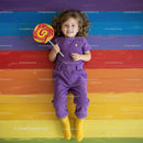 Happy child lying on colorful wooden floor with lollipop