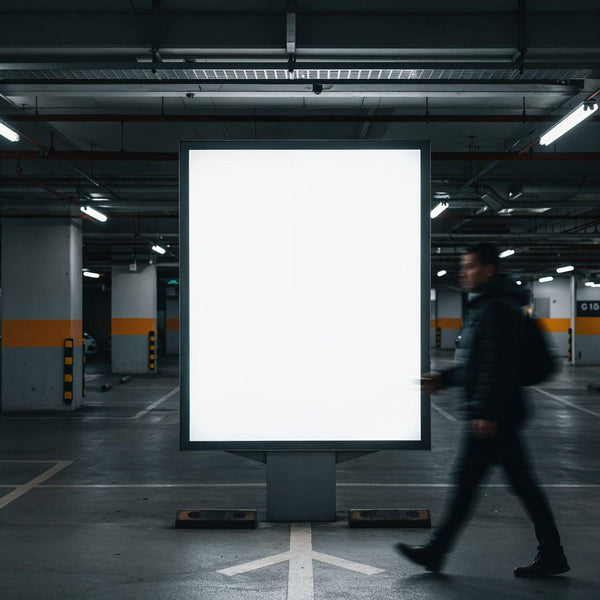 Man walking past illuminated blank billboard in parking garage JPG Mockup Image
