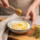 Honey Dripping from Wooden Dipper Over Yogurt in Cozy Kitchen