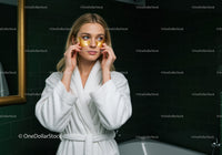 Young Woman in White Bathrobe Wearing Under Eye Patches in Bathroom