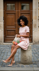 Smiling woman in pastel dress sitting with fruit bag