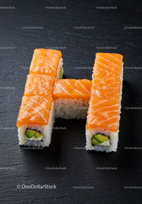 Fresh salmon sushi rolls arranged in letter H on dark surface