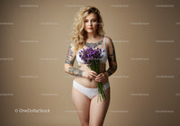Young Woman with Tattoos Holding Purple Flowers In Studio