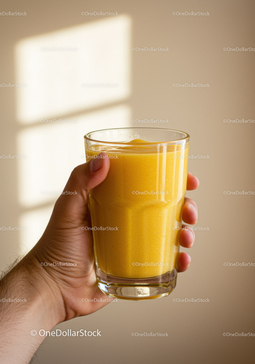 Dłoń trzymająca szklankę świeżego żółtego koktajlu mango
