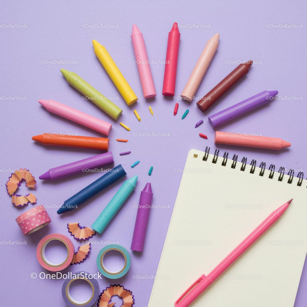 Colorful crayons and notebook on pastel background