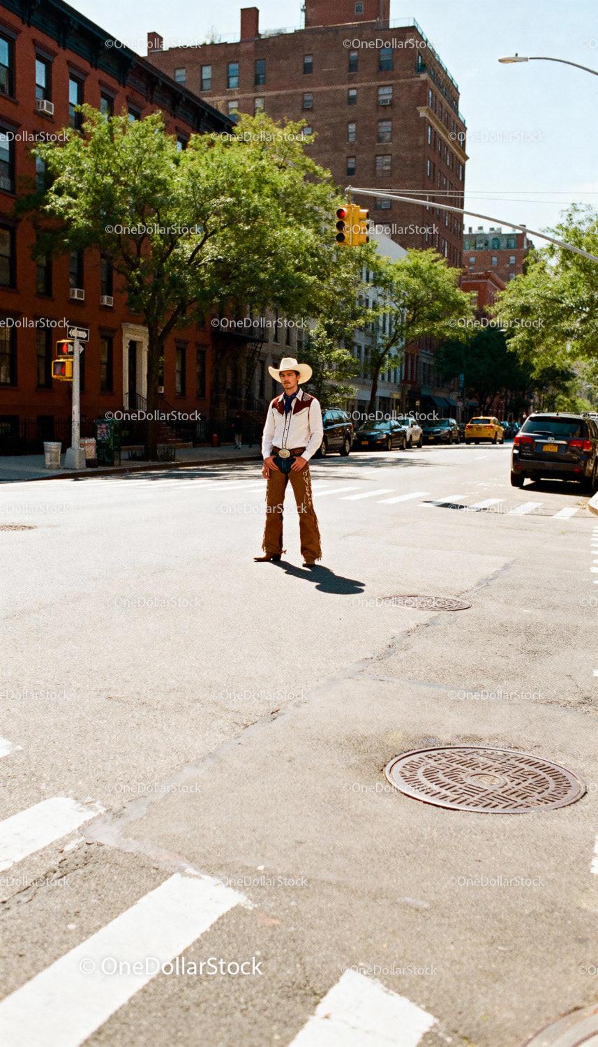 Man in cowboy outfit standing in urban street crossing