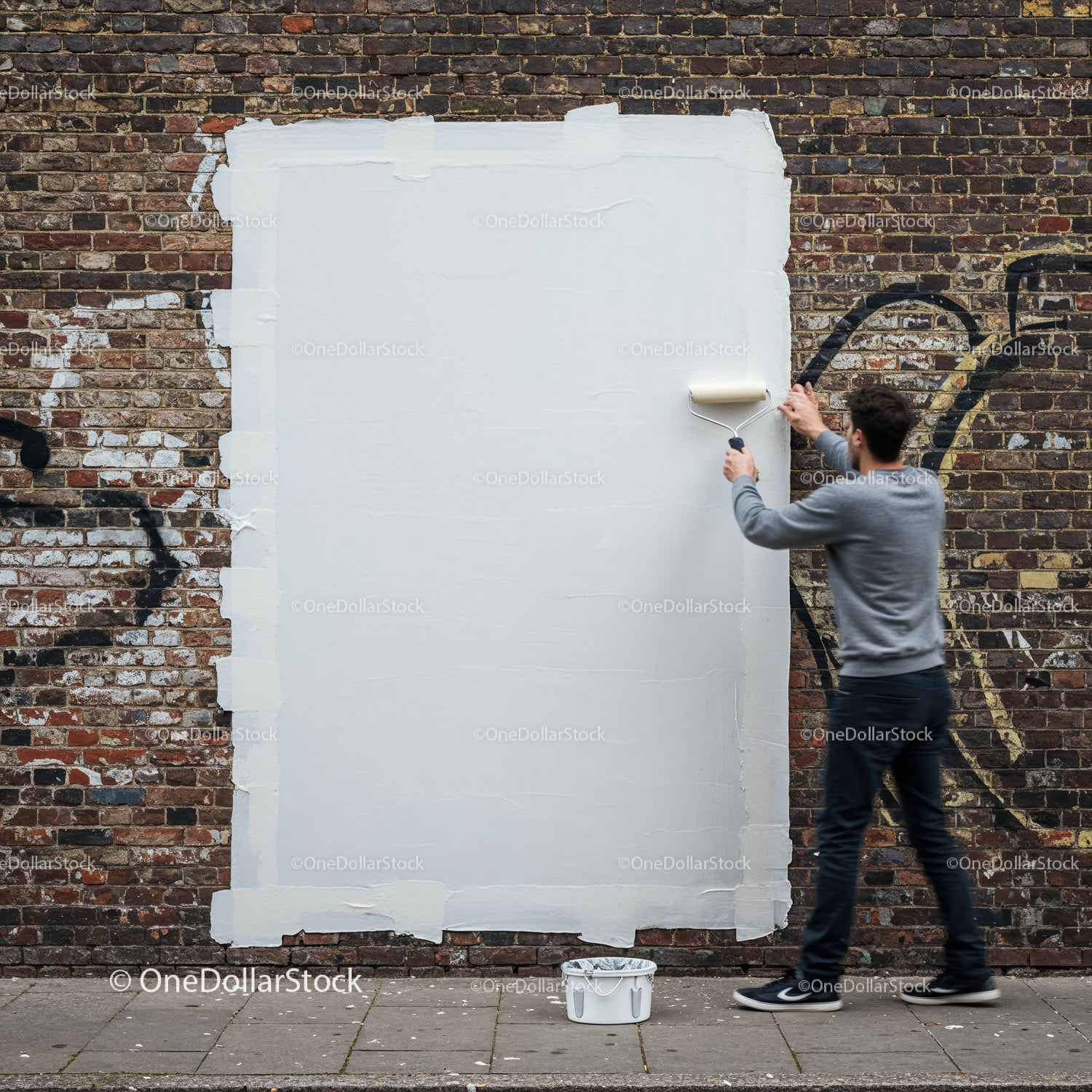 Mężczyzna zakrywający graffiti białą farbą na ścianie z cegły