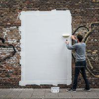 Man Covering Graffiti with White Paint on Brick Wall