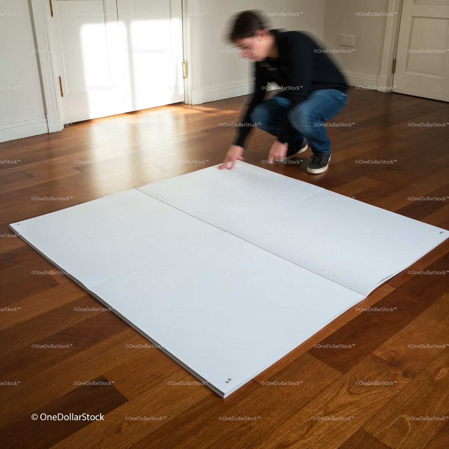 Man arranging large white panels on wooden floor indoors