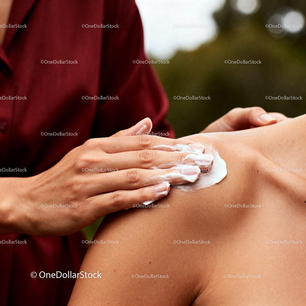 Hand applying soothing cream on woman’s shoulder outdoors