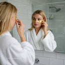 Young Woman Applying Eye Patches in Bathroom Mirror for Skin Care