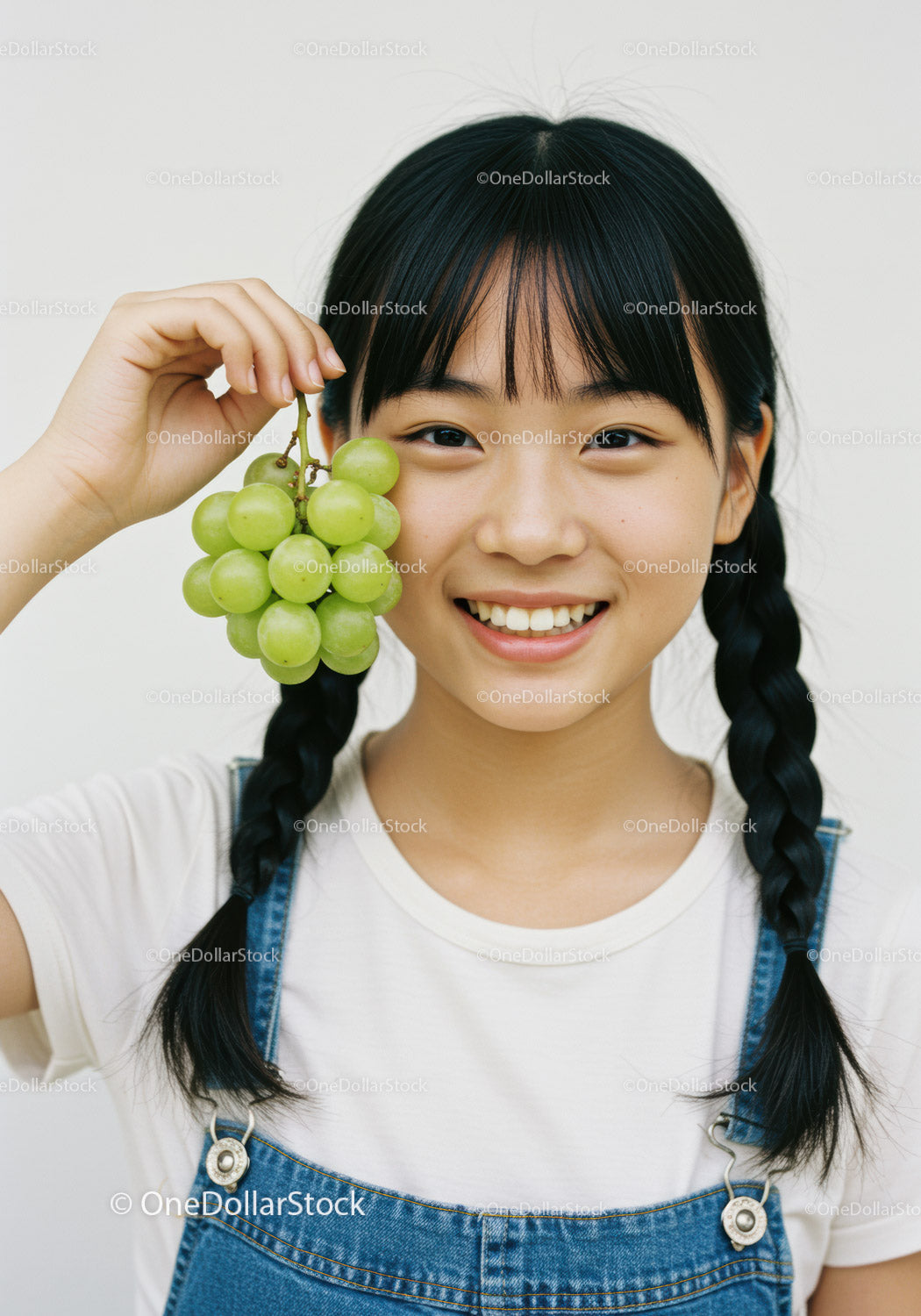 Smiling Girl with Braids Holding Fresh Green Grapes in Bright Setting