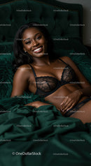 Smiling woman relaxing on green velvet bed in black lingerie