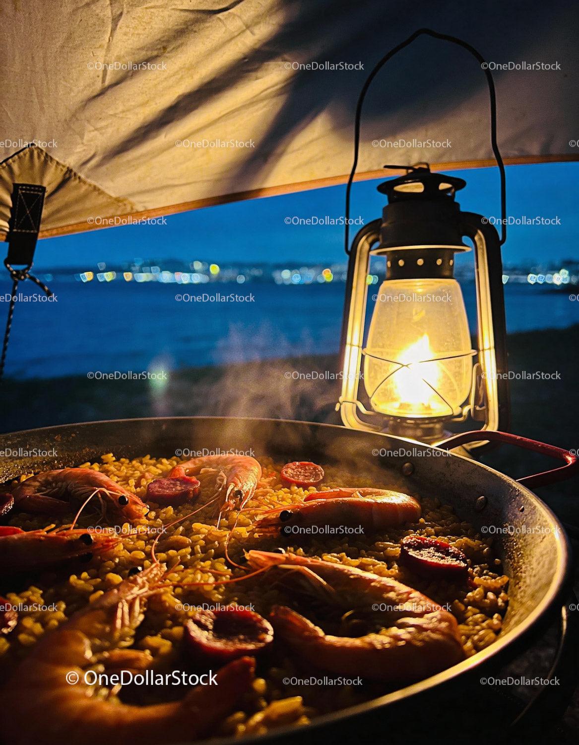 Seafood paella simmering by lantern light at dusk