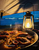 Seafood paella simmering by lantern light at dusk